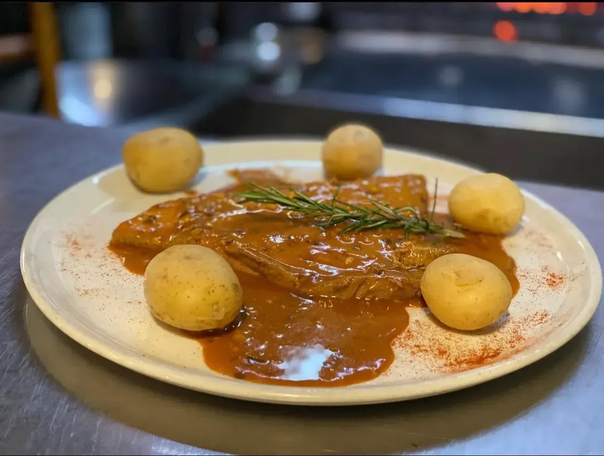 Plato de pescado en salsa con patatas pequeñas y ramita de romero.