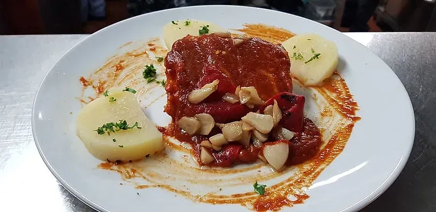 Plato de comida que incluye un plato de carne roja con salsa, ajo y rodajas de patata.