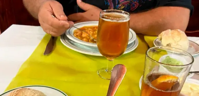 Persona comiendo en una mesa con cerveza, pan y salsa. Mantel amarillo.