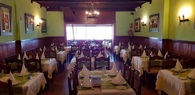 Interior de restaurante con mesas preparadas para cenar, paredes verdes y detalles en madera oscura.