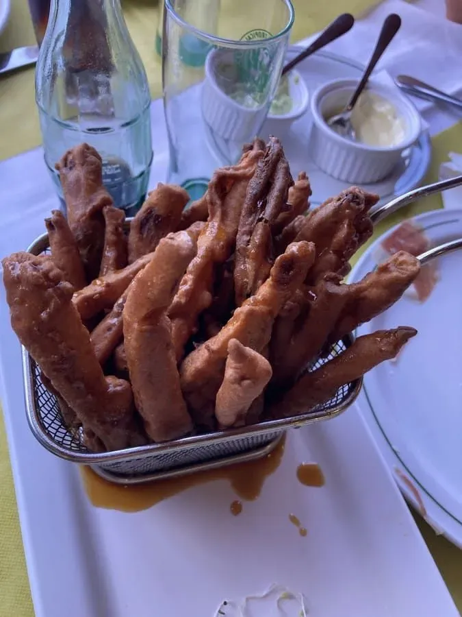 Comida frita en una cesta de alambre, con almíbar en el plato. Se ven la cristalería y los condimentos.