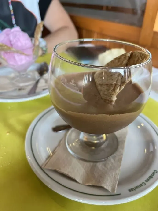 Postre en vaso, con galleta, sobre un plato con una servilleta de papel, sobre una mesa amarilla.