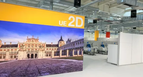 Gran pancarta con el logotipo 2D de la UE, imagen de un gran edificio, entorno interior con maquinaria y banderas.