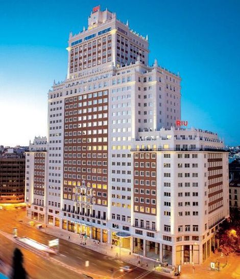 Hotel RIU Plaza España, Madrid, un gran edificio blanco con muchas ventanas, iluminado al anochecer.