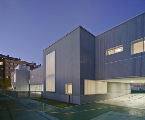 Edificio moderno gris con ventanas rectangulares, cancha deportiva al aire libre.