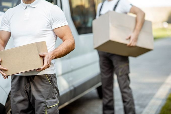 Dos repartidores llevan cajas delante de una furgoneta.
