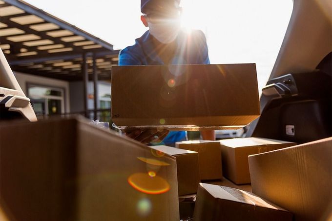 Un hombre que lleva una máscara está cargando cajas en la parte trasera de un automóvil.