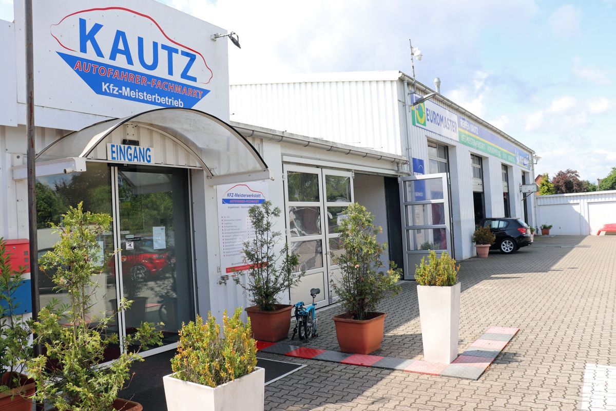KAUTZ Kfz-Werkstatt mit gläsernem Eingang, weißem Gebäude und Backsteinweg.