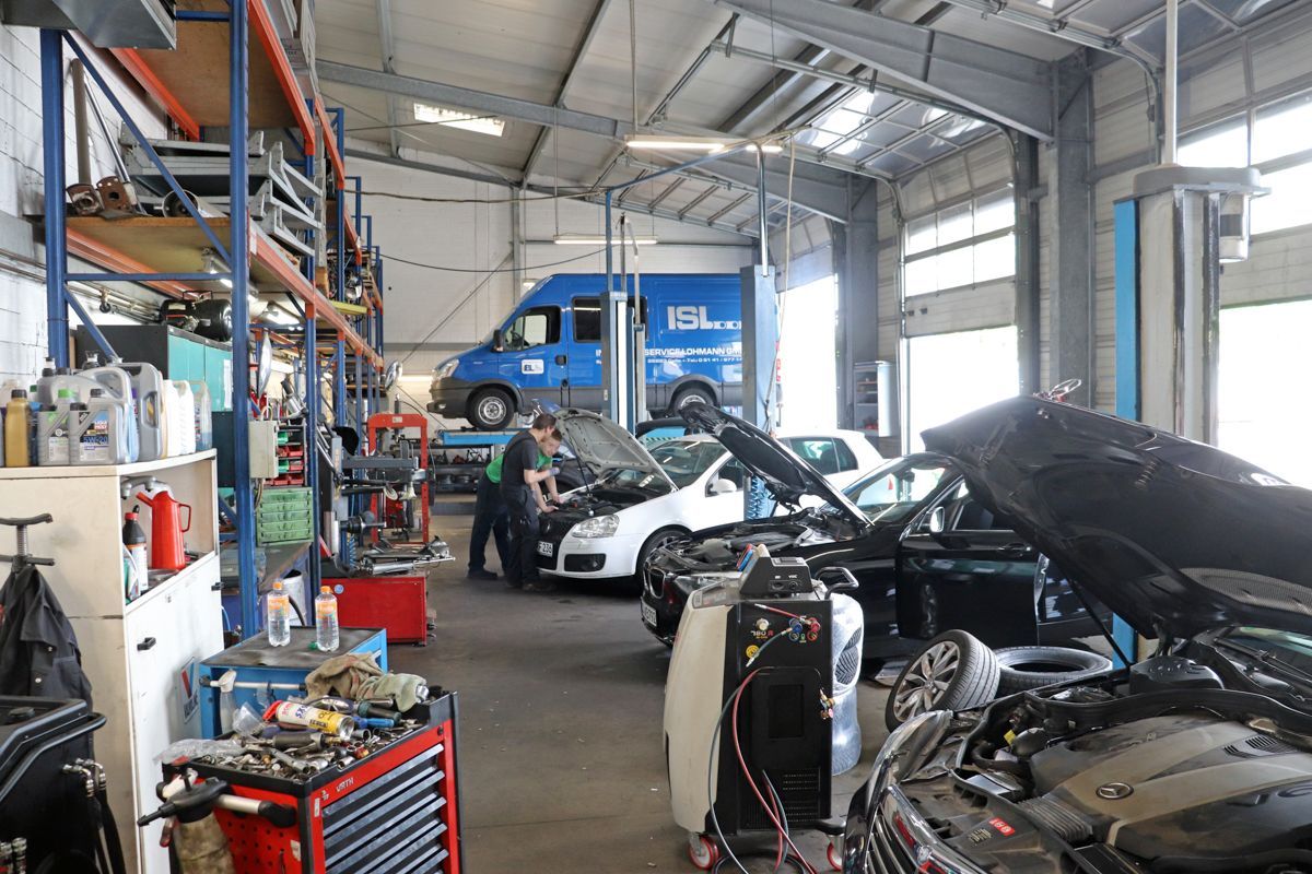 Innenansicht einer Autowerkstatt. Mechaniker arbeiten an Fahrzeugen mit geöffneten Motorhauben.