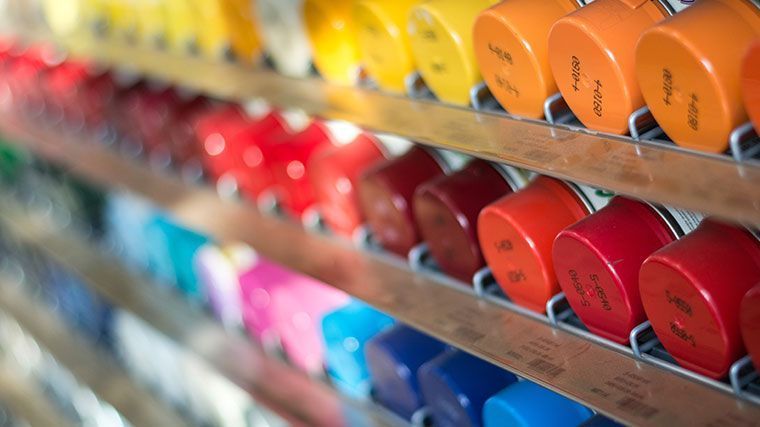 Reihen von bunten Farbdosen auf einem Regal, von Gelb über Rot bis Blau.