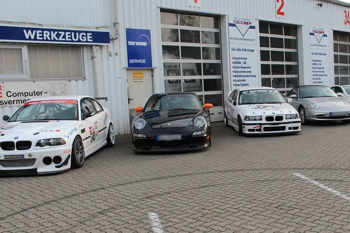 Vor einer Garage parkten mehrere Autos, darunter ein schwarzer Porsche, zwei BMWs und ein silberner Wagen.
