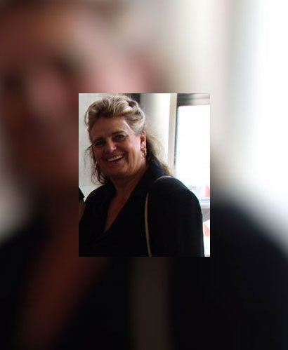 Frau lächelt, ist schwarz gekleidet und befindet sich in einem Innenraum, möglicherweise bei einer Veranstaltung.