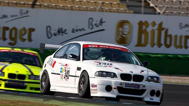 Zwei BMW-Rennwagen auf der Rennstrecke; einer weiß mit Heckflügel, einer gelb. Im Hintergrund ein „Bitburger“-Schild.