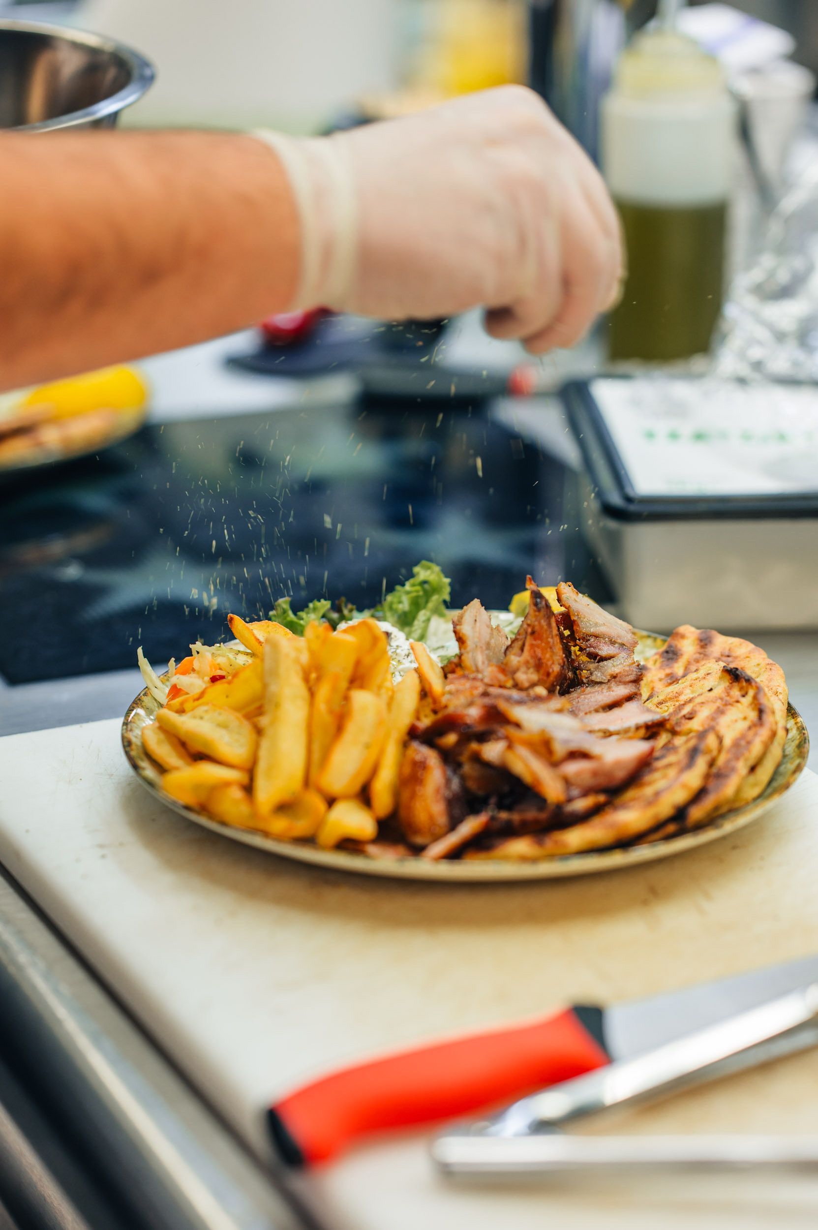Der Koch bestreut einen Teller mit gegrilltem Fleisch, Pommes frites und Salat mit Gewürzen.