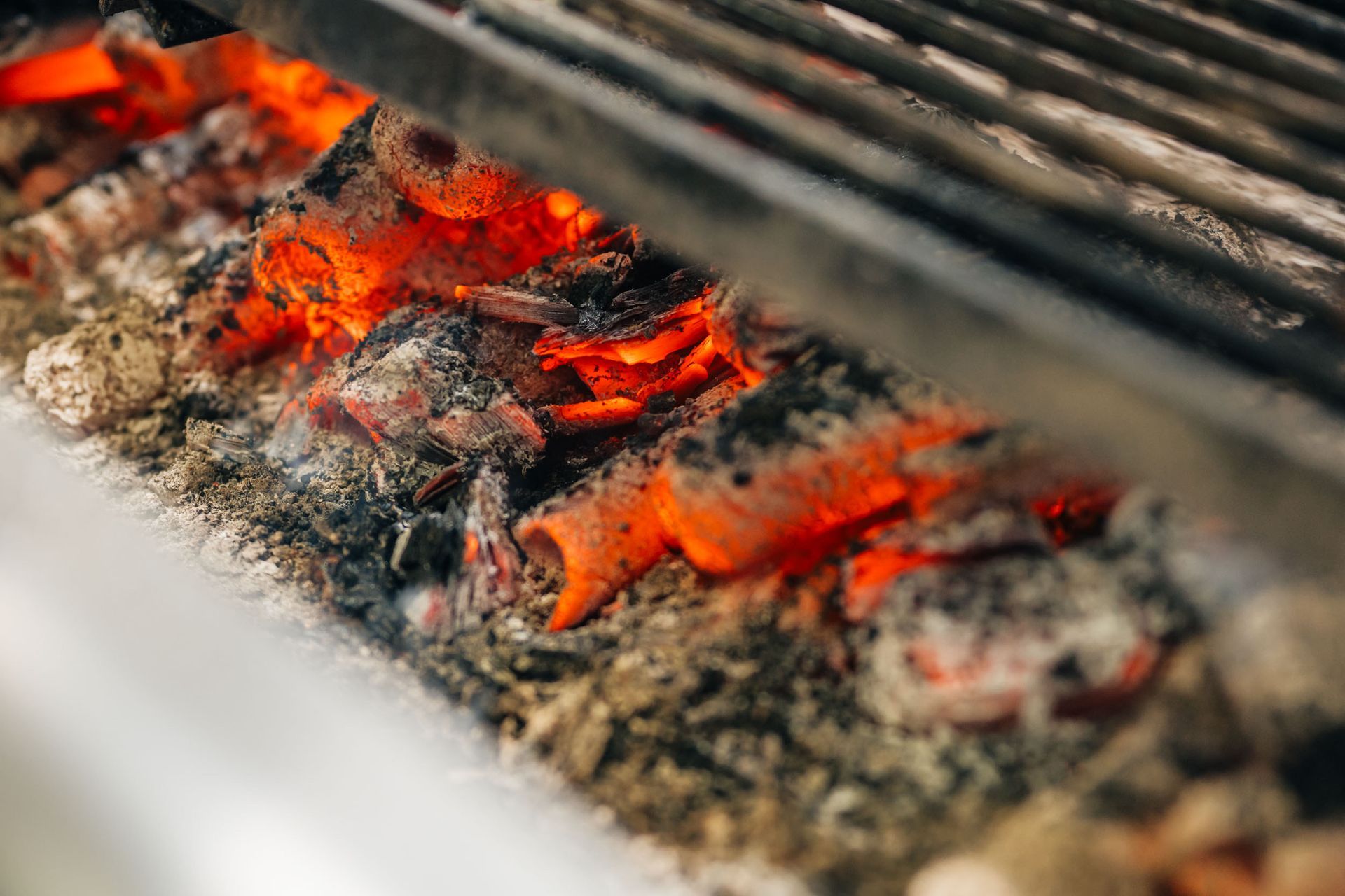 Glühende Glut unter einem Grillrost; Nahaufnahme mit leuchtend orangefarbenen und grauen Farbtönen.