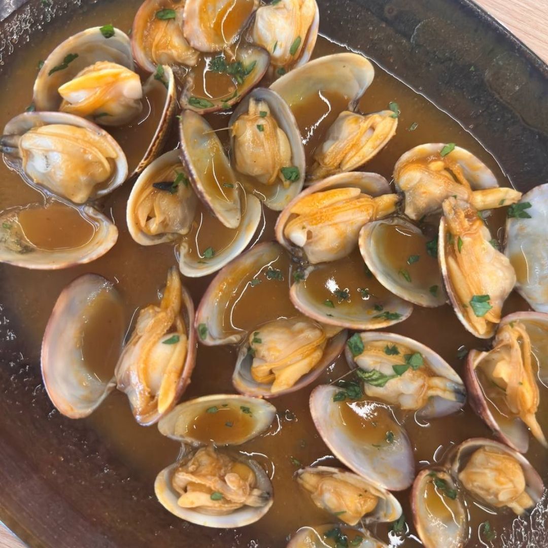 Almejas en salsa marrón, adornadas con perejil, servidas en un plato rectangular.