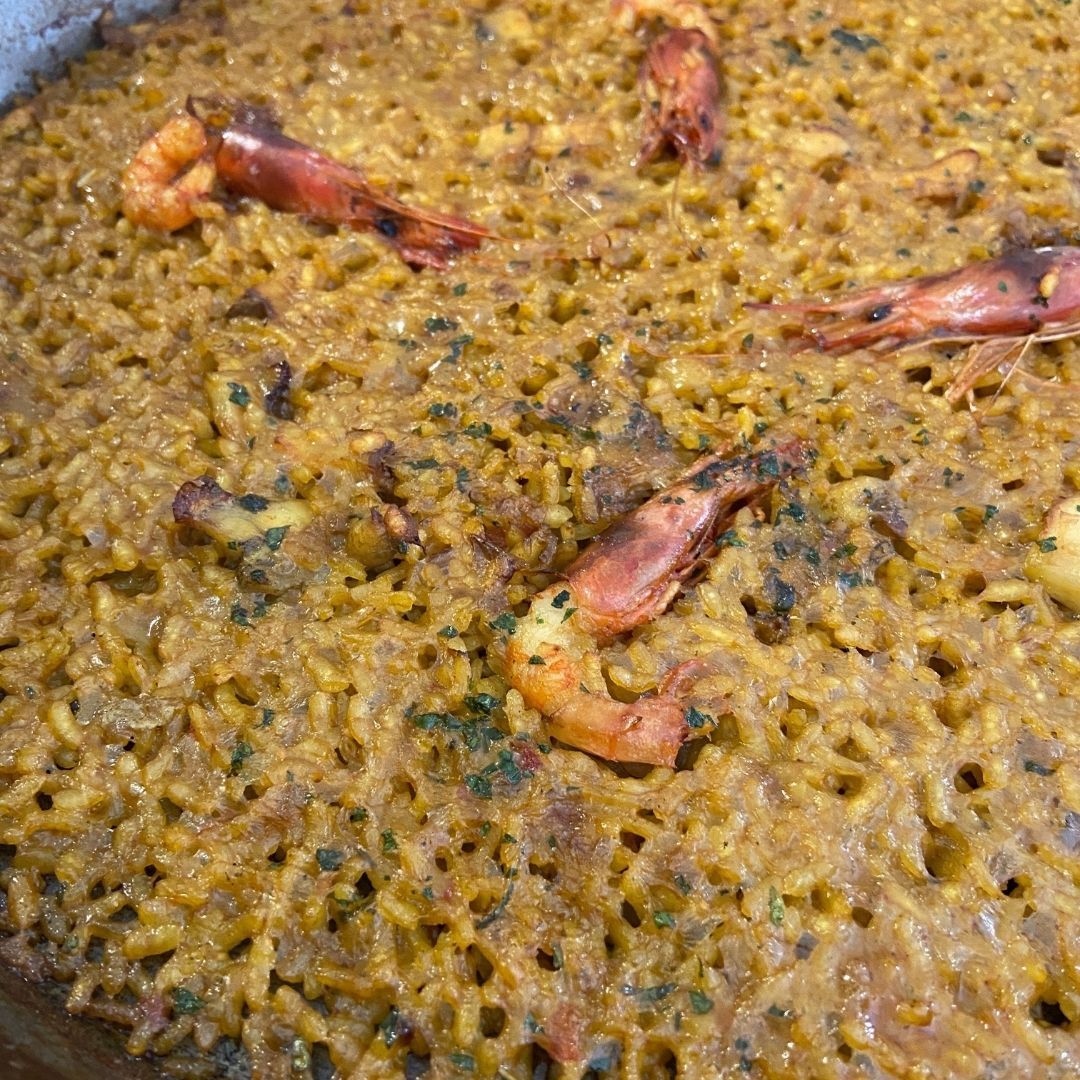 Paella con camarones, arroz dorado y hierbas en una sartén grande.
