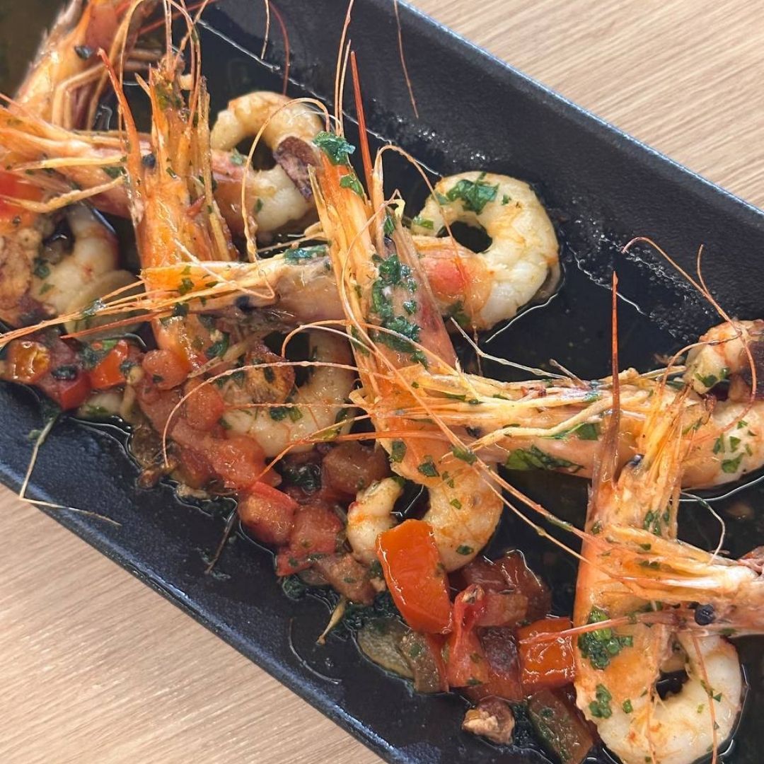 Plato de camarones en plato negro, adornado con hierbas y verduras de colores.