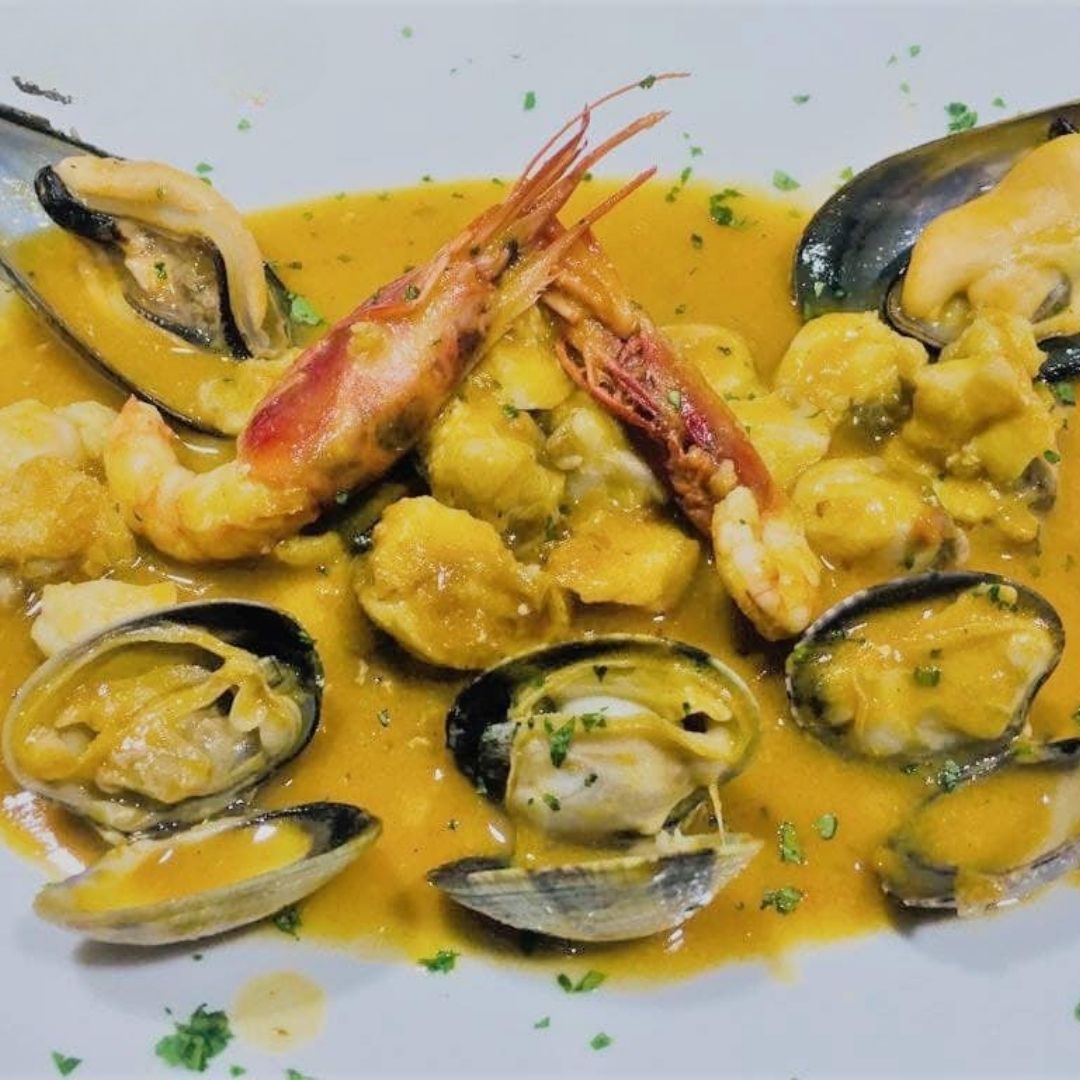 Plato de mariscos con mejillones, camarones, almejas y salsa amarilla.