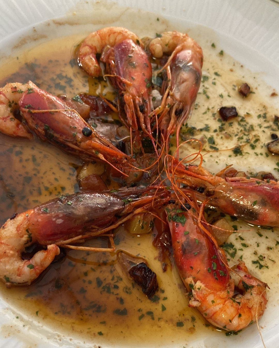 Seis camarones cocidos en un plato en un charco de salsa, adornados con hierbas.