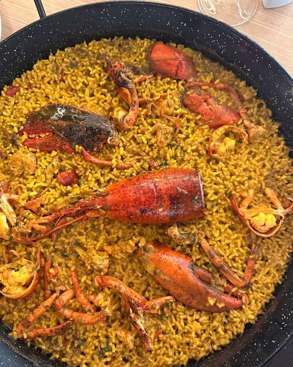 Paella con bogavante, arroz amarillo en sartén grande.