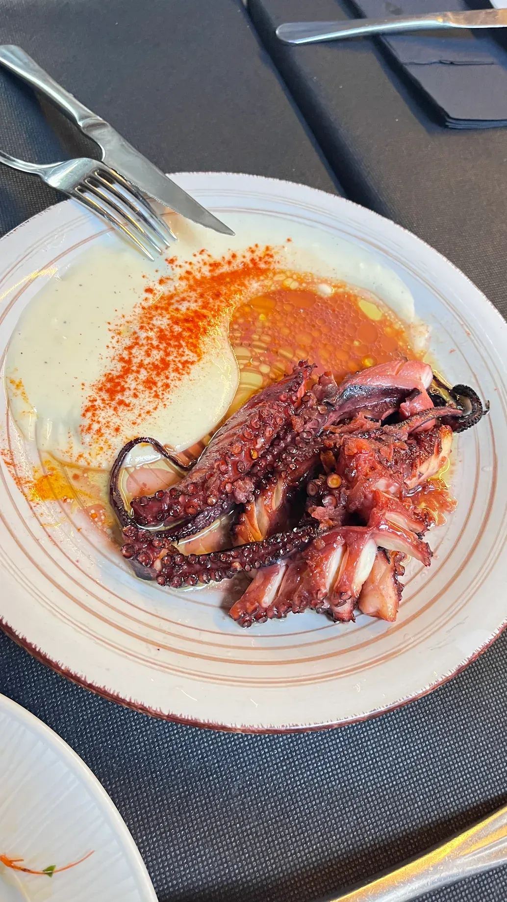 Pulpo a la plancha con puré de patatas y pimentón, en plato blanco.