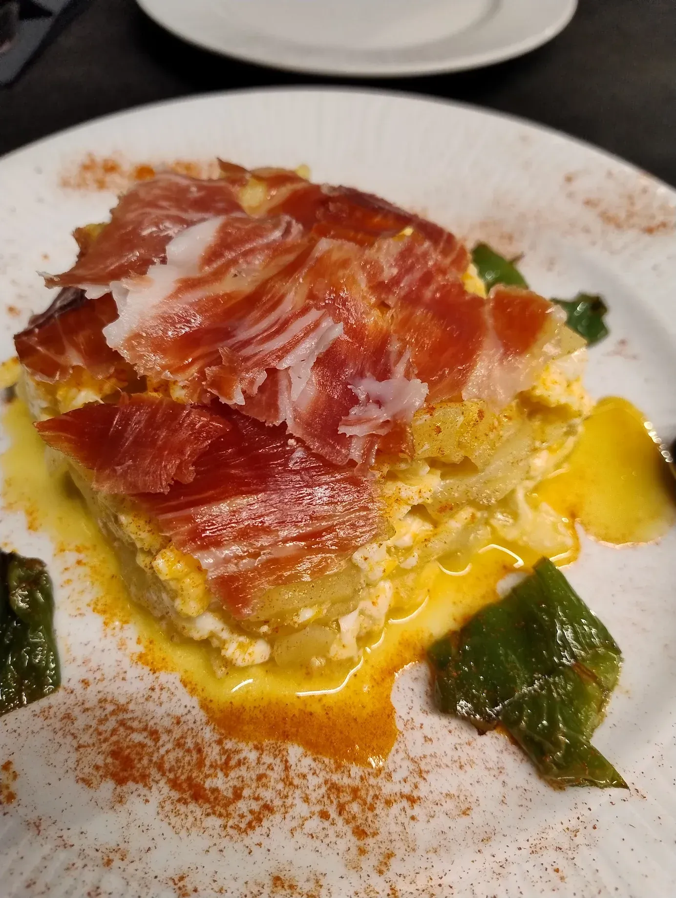 Cazuela de patatas y huevos con jamón, pimentón y pimientos en un plato blanco.