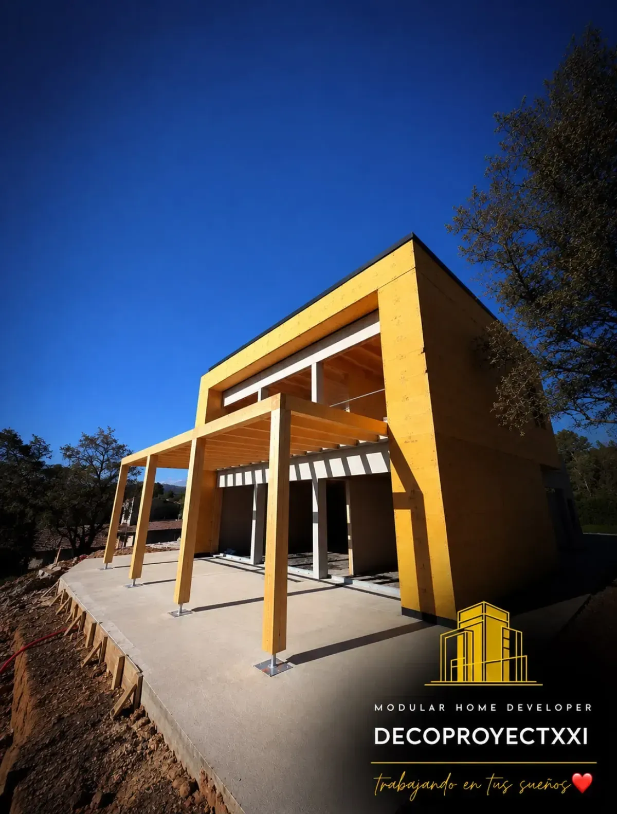 Exterior de una casa moderna de color amarillo con porche y altas columnas bajo un cielo azul despejado.
