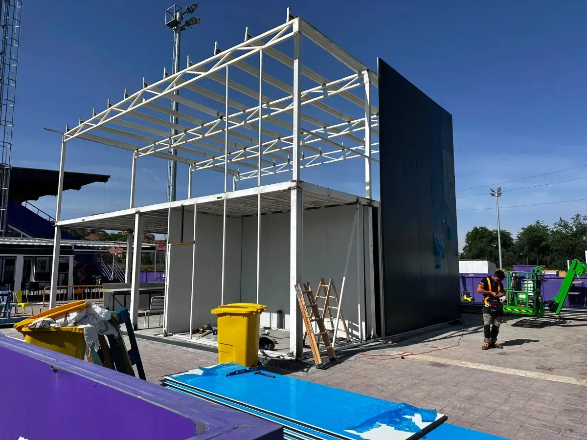 Estructura blanca parcialmente construida con armazón de metal, panel azul y materiales de construcción en el exterior.