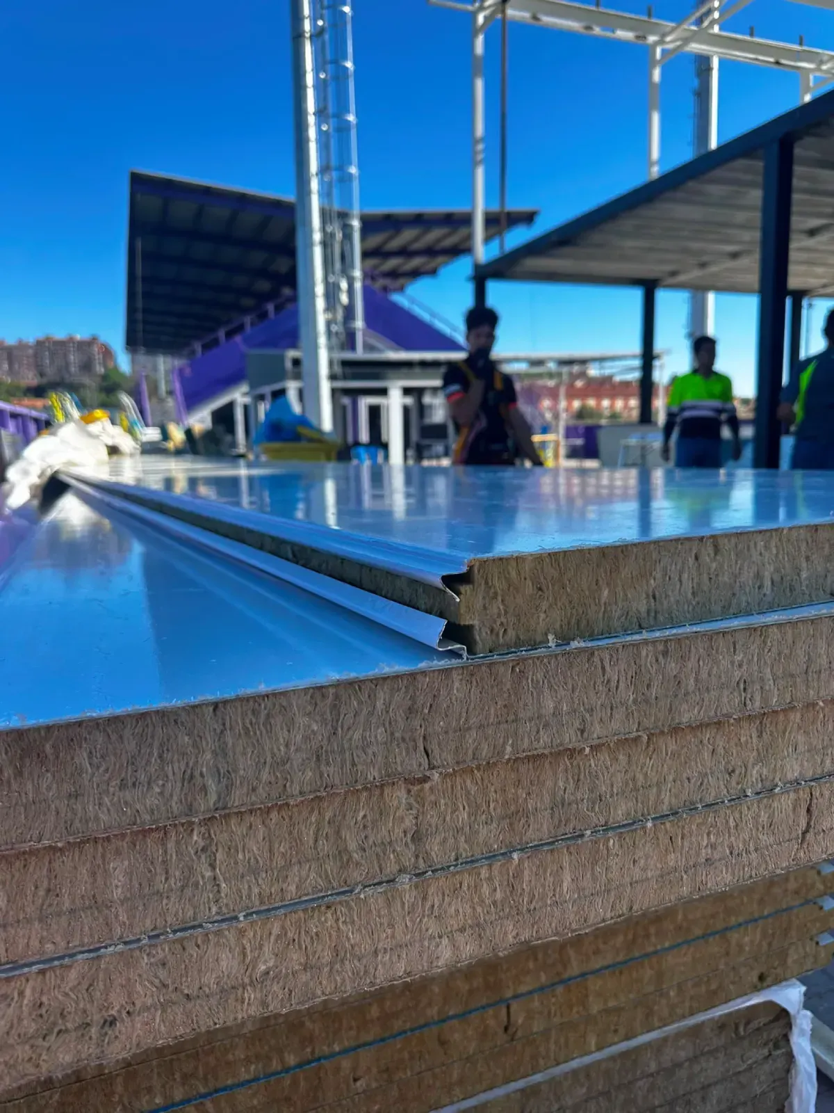 Piscina en la azotea con agua azul y gente de pie bajo un toldo azul brillante en un día soleado.