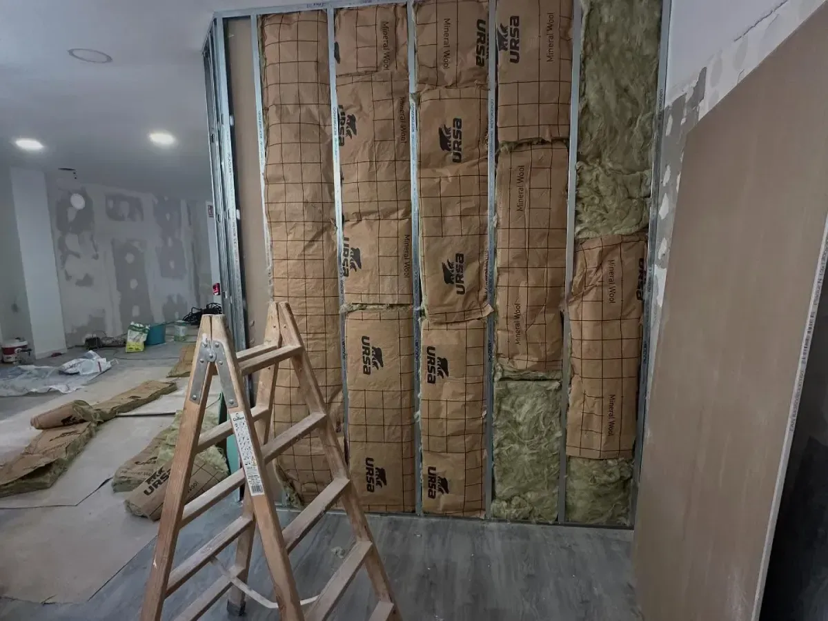 Reforma interior con aislamiento expuesto, escaleras y materiales de construcción en una habitación en reparación.