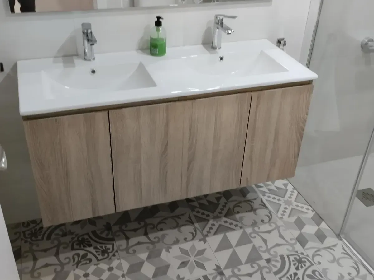 Tocador de baño moderno con doble lavabo, encimera blanca, mueble de madera y suelo de baldosas estampadas.