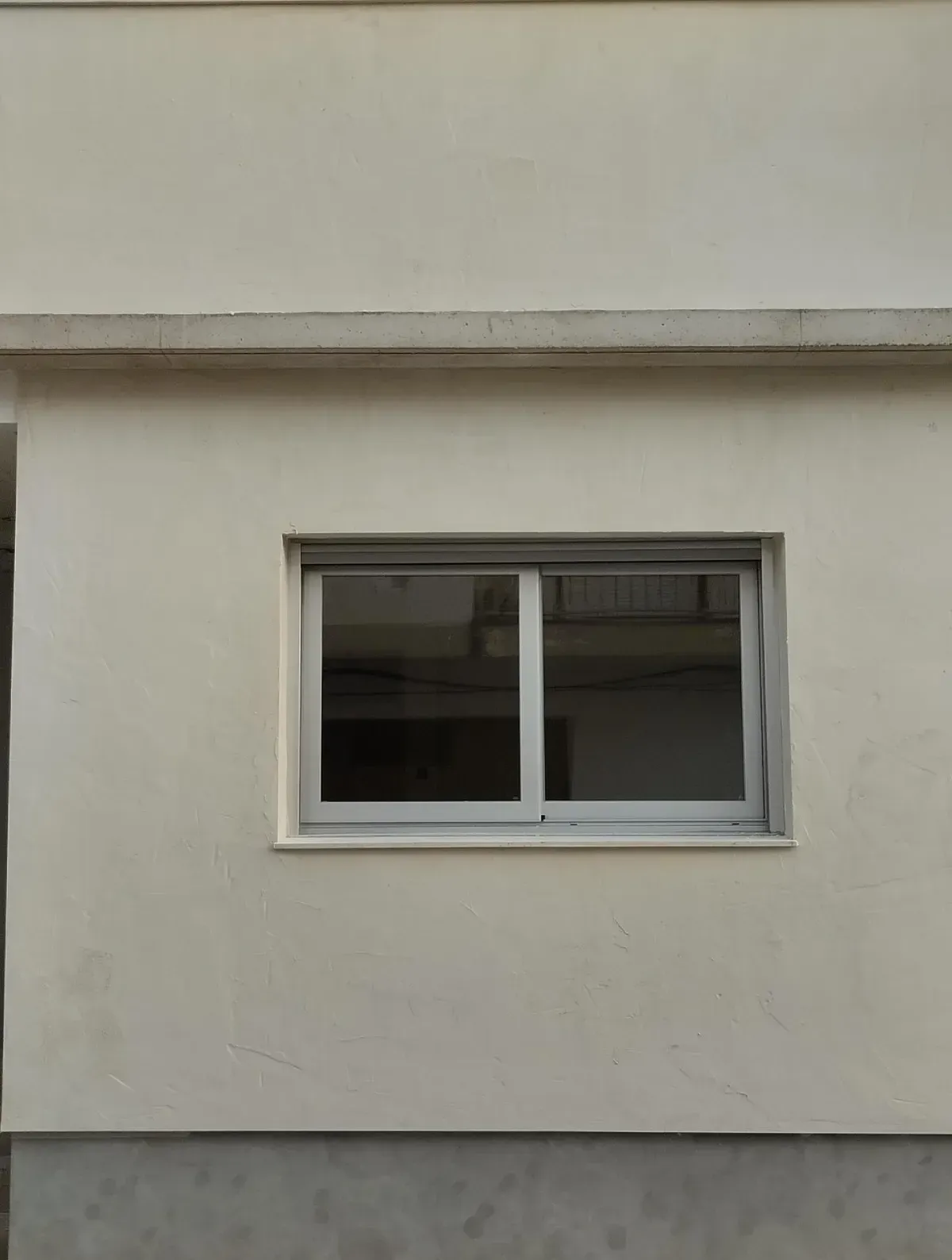 Pared blanca del edificio con una pequeña ventana corredera rectangular.
