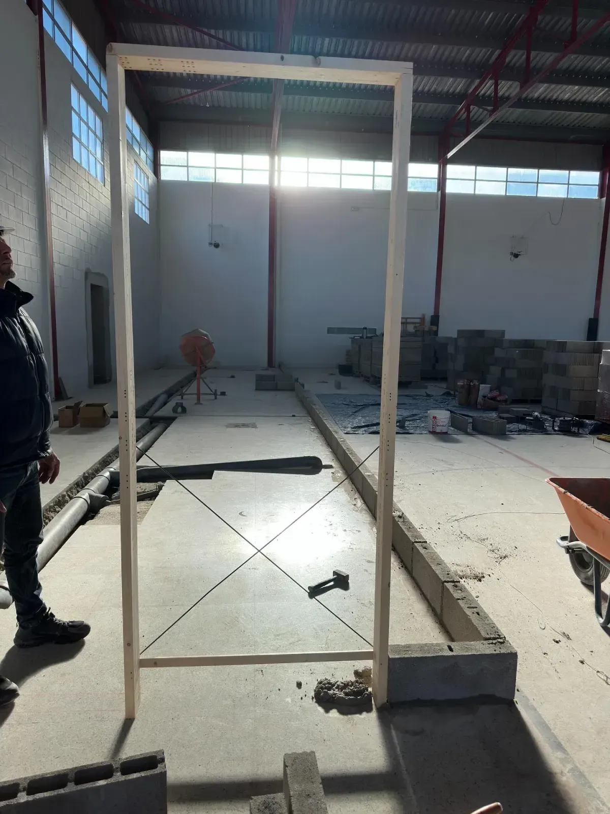 Un hombre se encuentra de pie en un almacén en construcción con suelo de hormigón, andamios y bloques apilados.