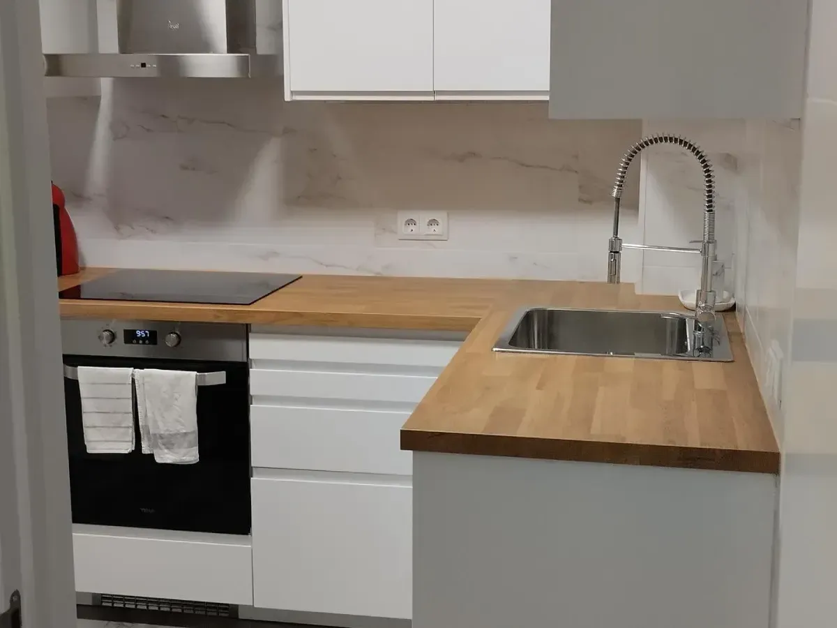 Cocina moderna y compacta con gabinetes blancos, encimeras de madera, estufa, fregadero y grifo de acero inoxidable.