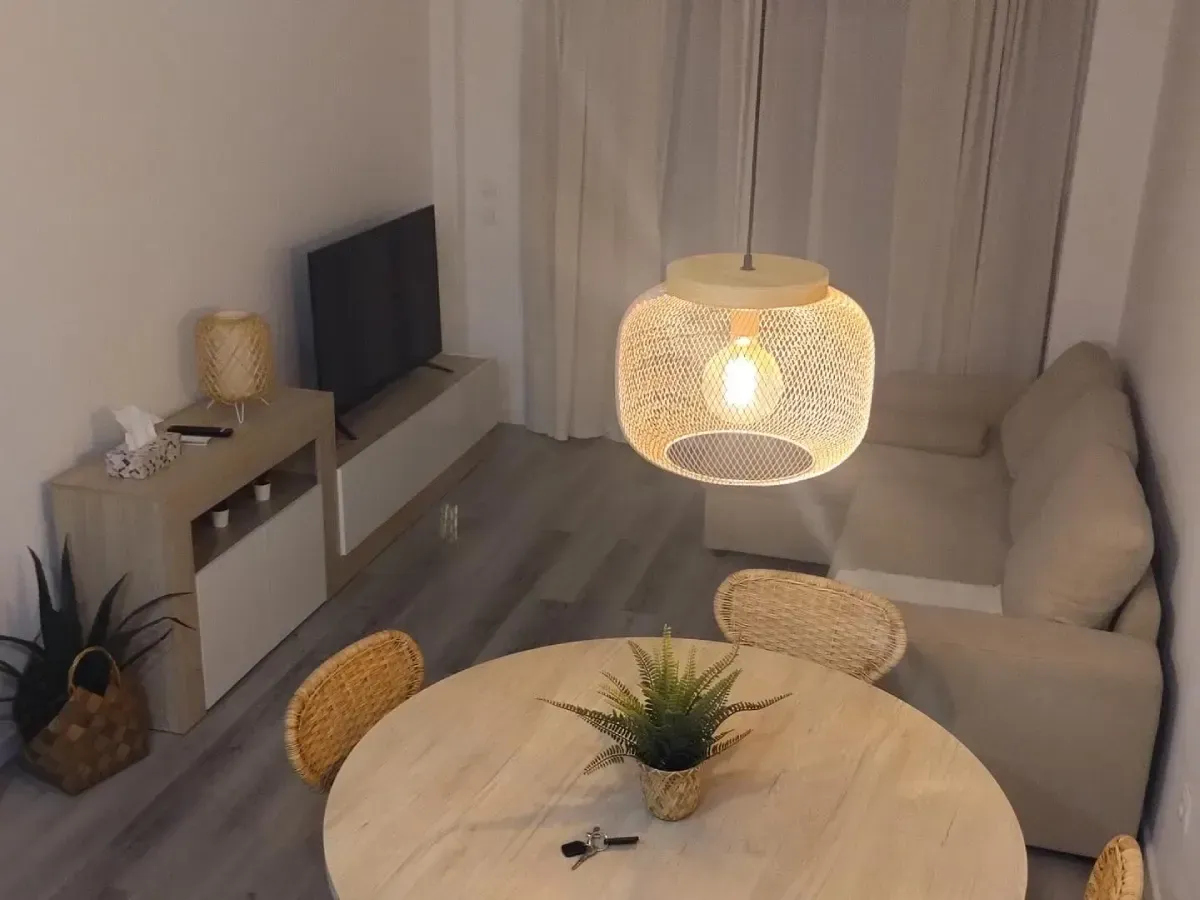 Acogedora sala de estar con sofá beige, mesa de comedor redonda, mueble para TV y lámpara colgante de mimbre.