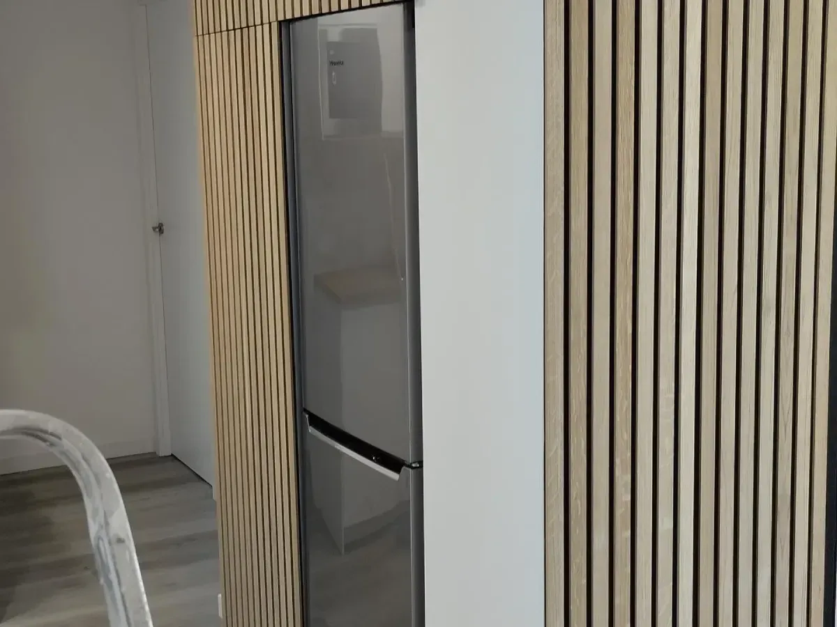 Refrigerador de acero inoxidable entre paneles de pared a rayas en una cocina moderna.