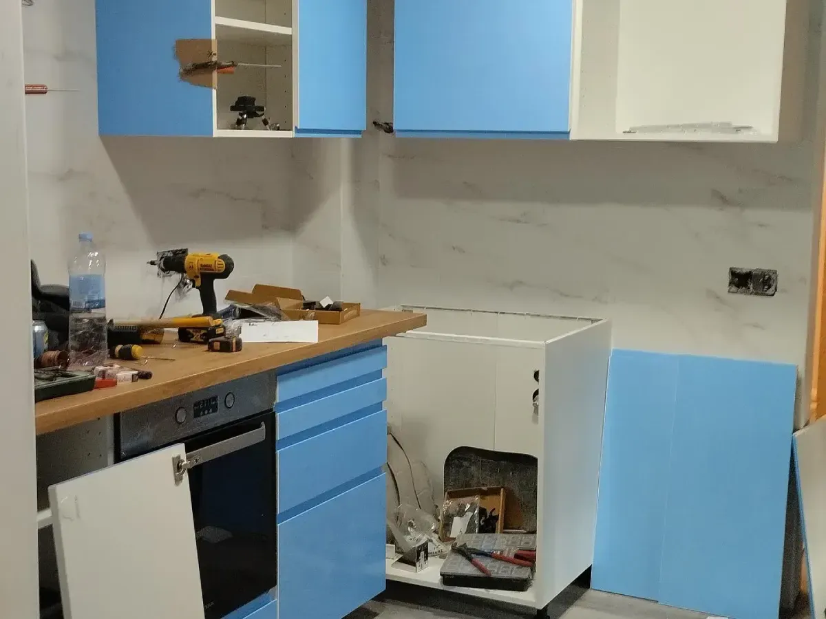 Cocina parcialmente renovada con gabinetes azules, encimera de madera, utensilios y un armario debajo del fregadero abierto.