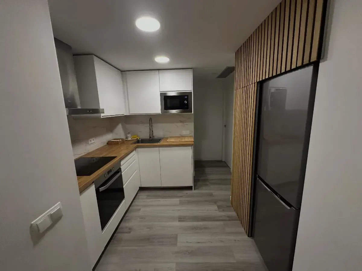 Cocina moderna con gabinetes blancos, encimeras de madera, piso gris y electrodomésticos de acero inoxidable.