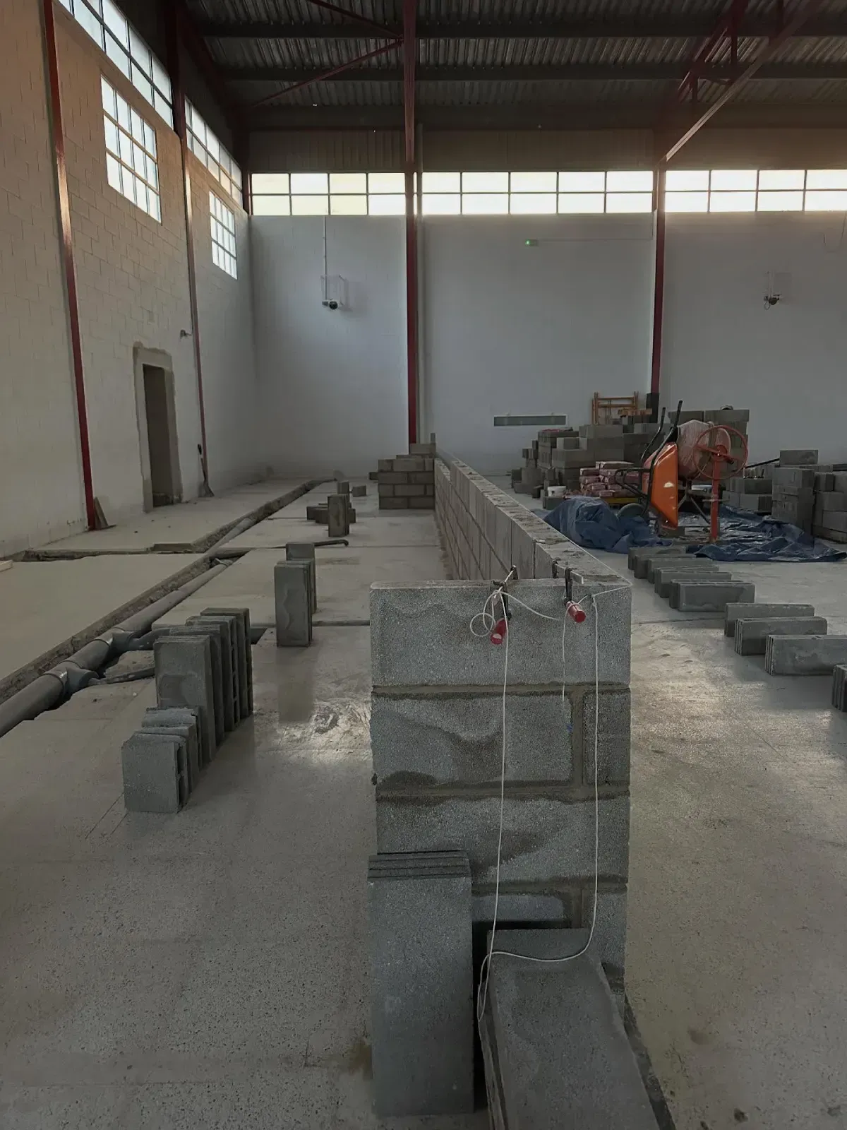 Almacén interior con pilas de bloques de hormigón gris y un trabajador cerca de maquinaria al fondo.