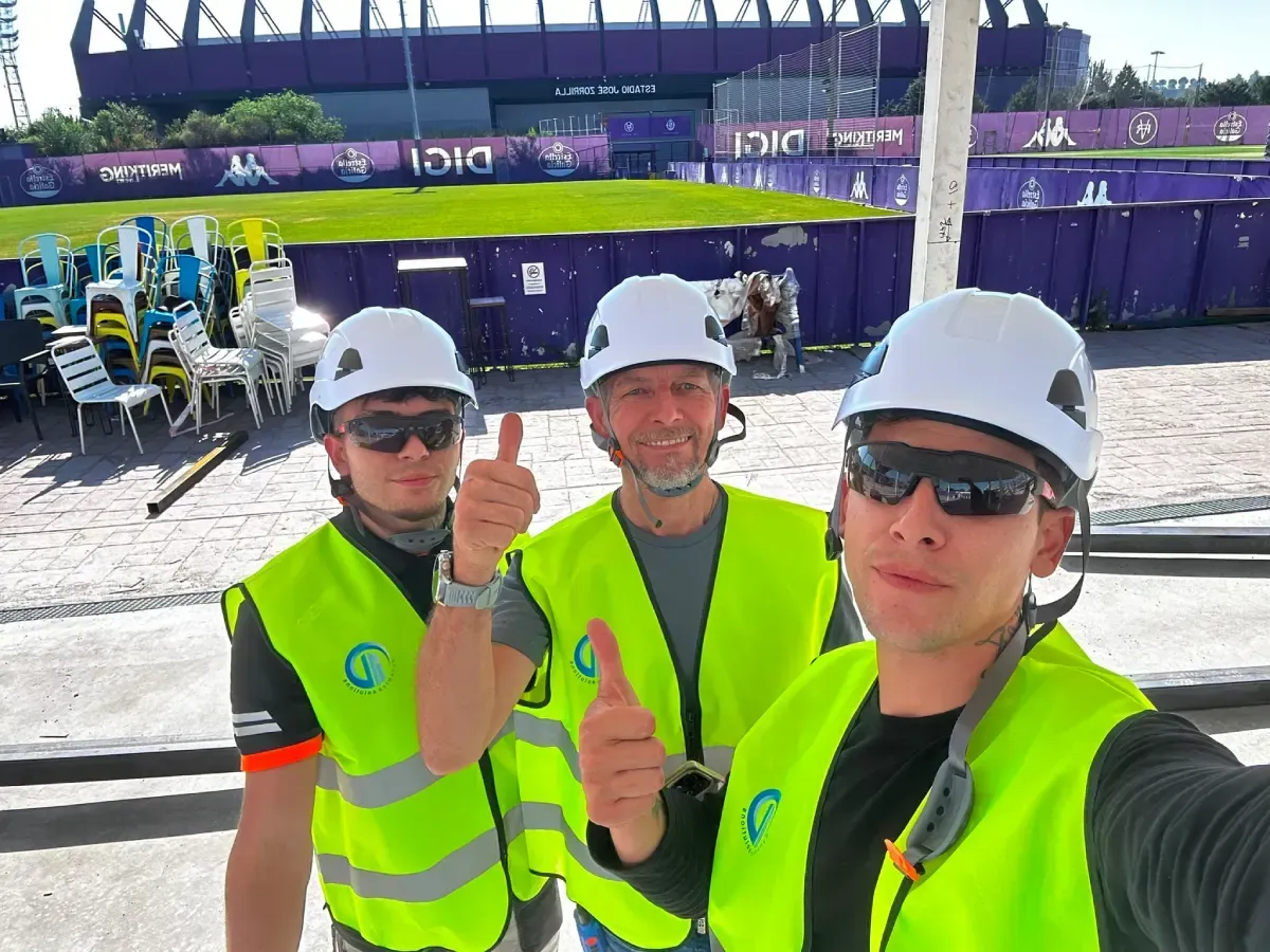 Tres trabajadores con chalecos reflectantes de seguridad y cascos posan en un evento al aire libre