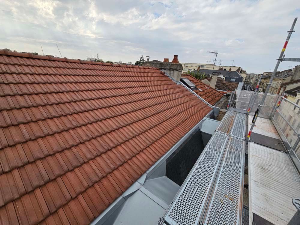 Toit de tuiles rouges avec échafaudages à côté, ciel nuageux en arrière-plan.