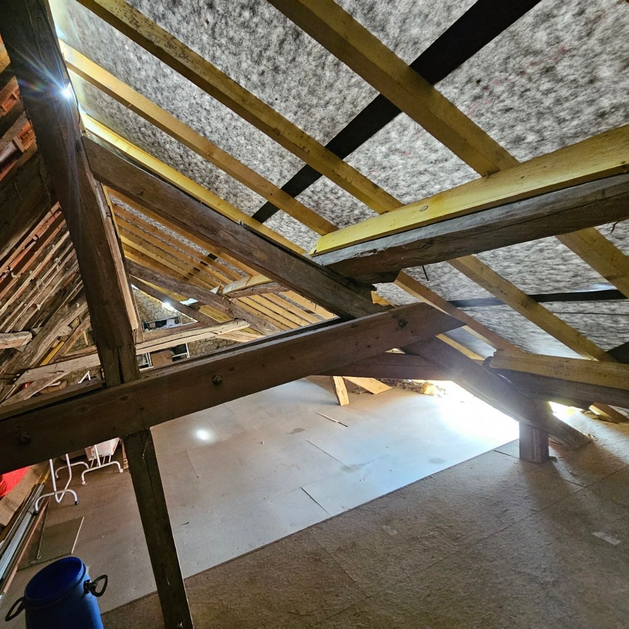 Intérieur de combles en bois avec poutres apparentes et isolation visible.