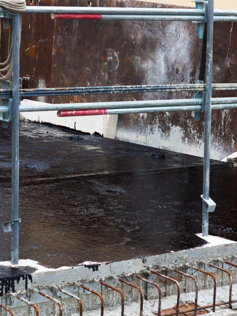 Échafaudage métallique sur un toit sombre ; une corniche en béton est visible au premier plan.