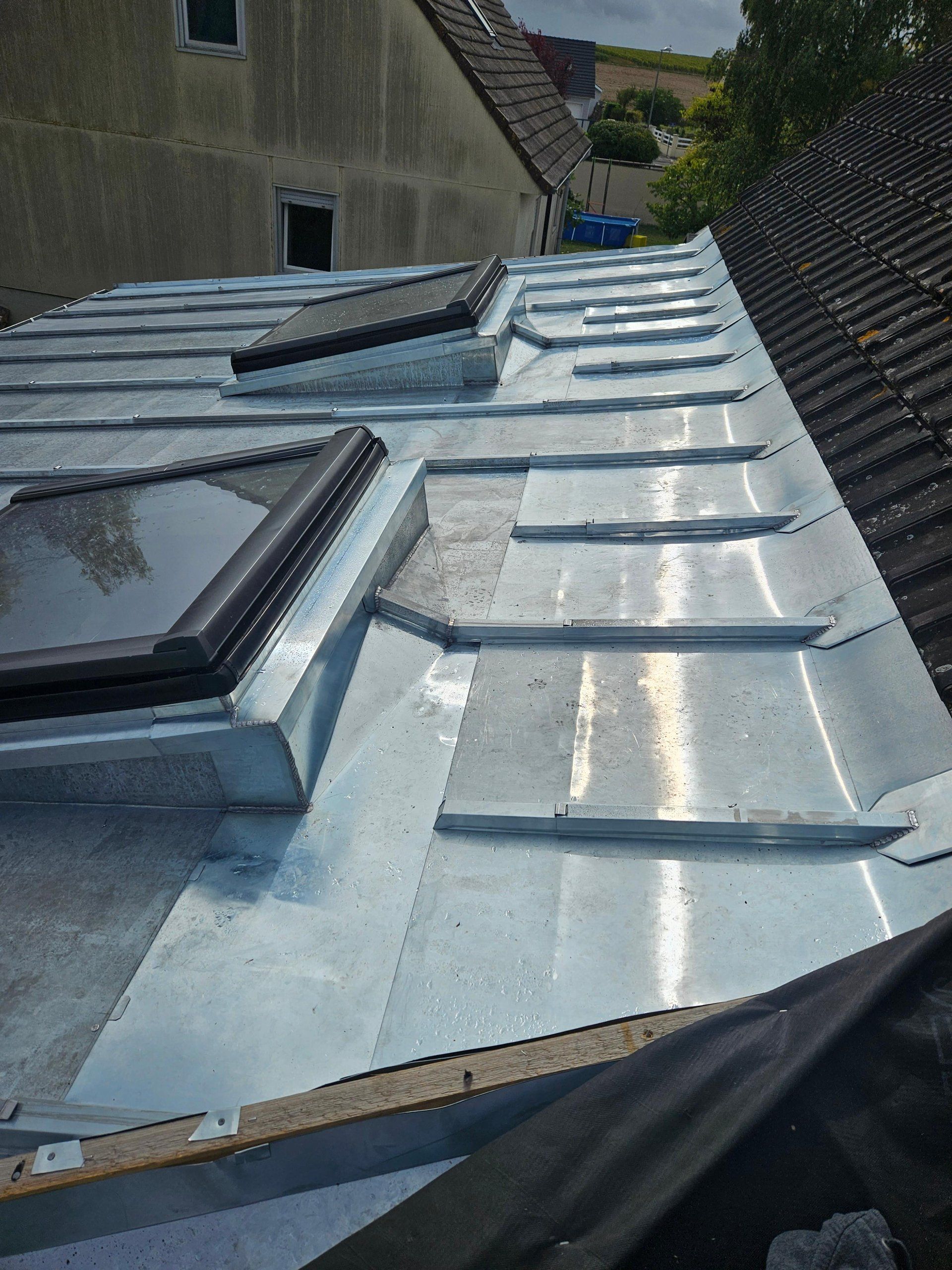 Toiture métallique percée de deux puits de lumière. La lumière du soleil se reflète sur les surfaces argentées du toit.