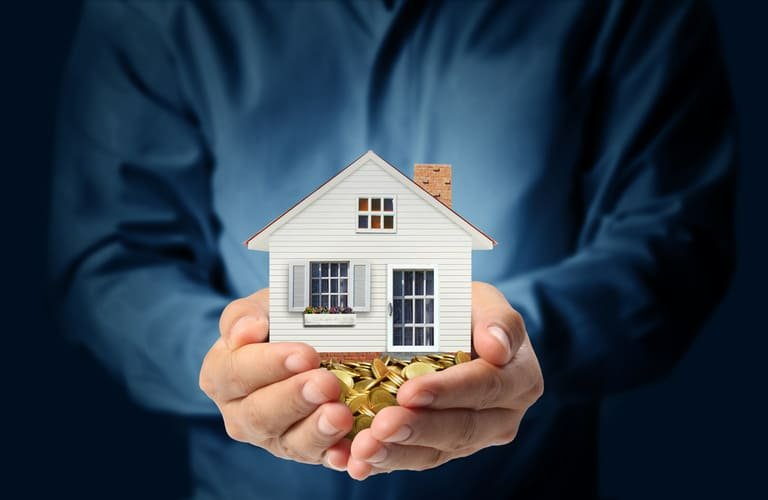 Un hombre sostiene una casa modelo y monedas en sus manos.