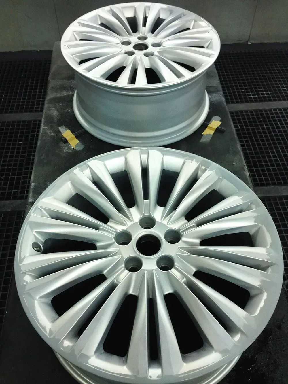 Zwei silberne Autofelgen, frisch lackiert, liegen auf einer schwarzen Fläche.