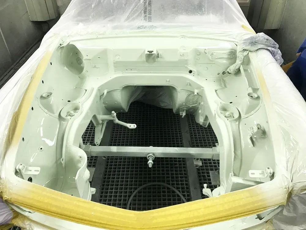 Motorraum eines hellgrün lackierten Autos, abgedeckt mit Plastikfolie und Klebeband in einer Lackierkabine.