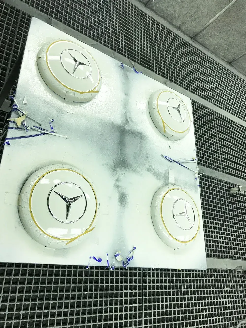 Eine Tafel mit vier weißen Mercedes-Benz-Radkappen, die in einer Werkstatt lackiert wurden.