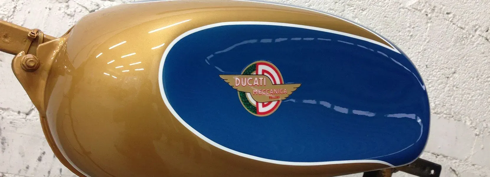 Goldener Motorrad-Benzintank mit blauem Akzent und Ducati-Logo.